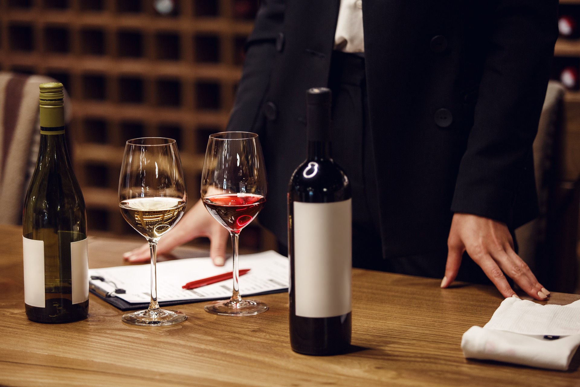 Opened bottles with filled glasses of red and white wine at the table on person hands background, close up. Teacher of winemaking preparing starts training beginners professionals.